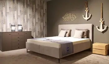 Modernes Schlafzimmer mit gepolstertem Doppelbett, dekorativen Kissen, passender Kommode, Nachttisch und maritimer Wanddekoration mit Ankern in warmem, gemütlichem Ambiente.